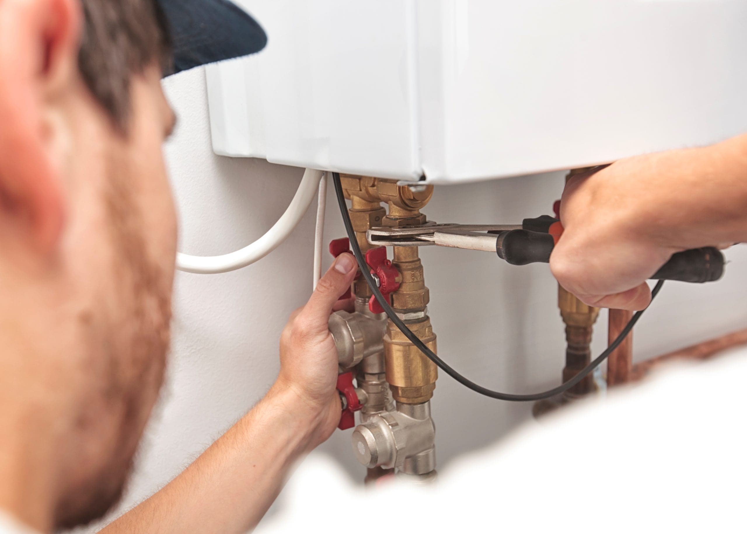 Person repairing or installing a boiler with a wrench, adjusting pipes and valves. Close-up view of hands working on plumbing with focus on tools and connections.