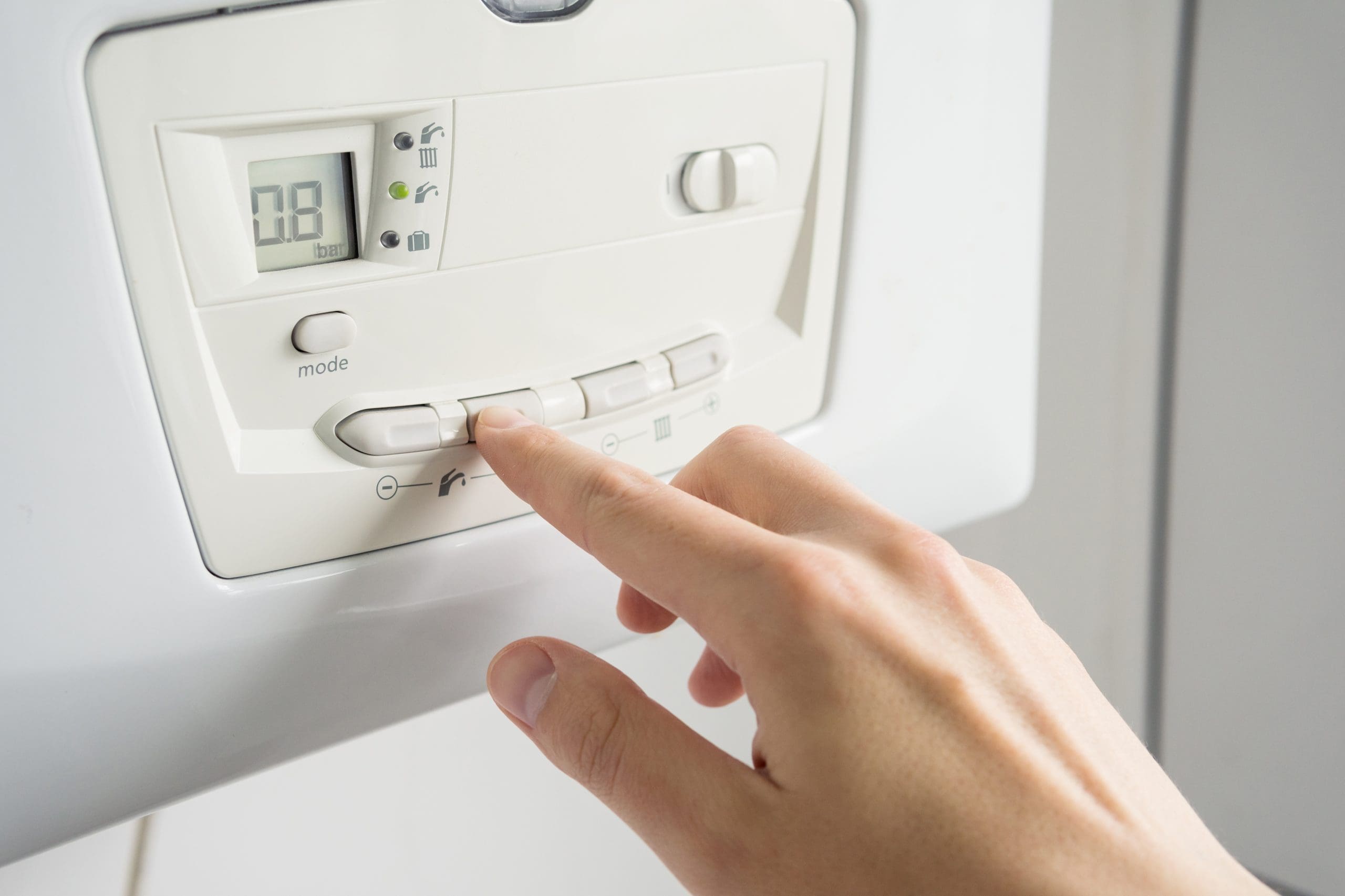 A person adjusts the settings on a white boiler control panel, showing a digital display and several buttons. The hand is pressing a button while the screen displays "08.