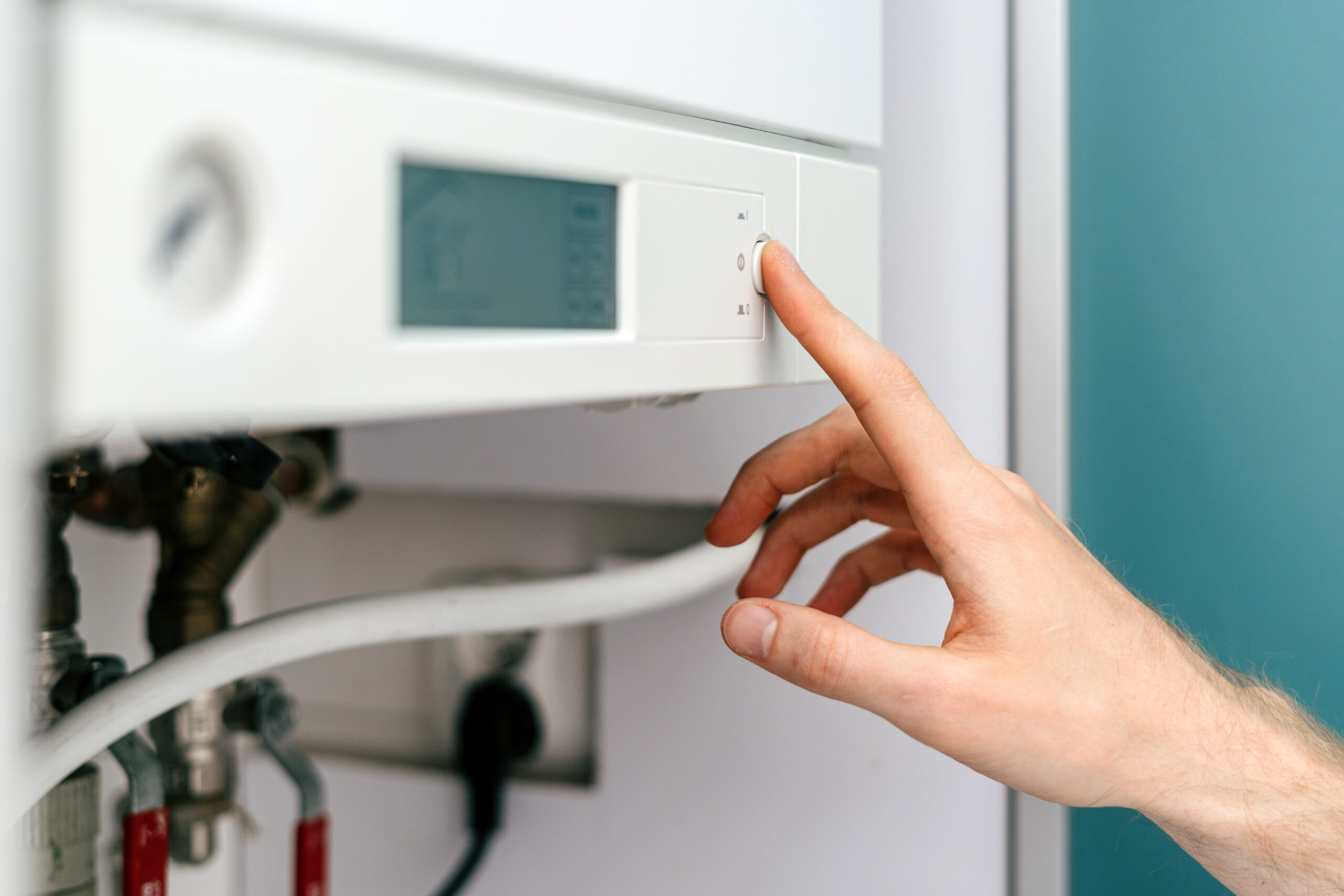 A close-up of a person’s hand adjusting the control knob on a white wall-mounted thermostat or boiler with a digital display.