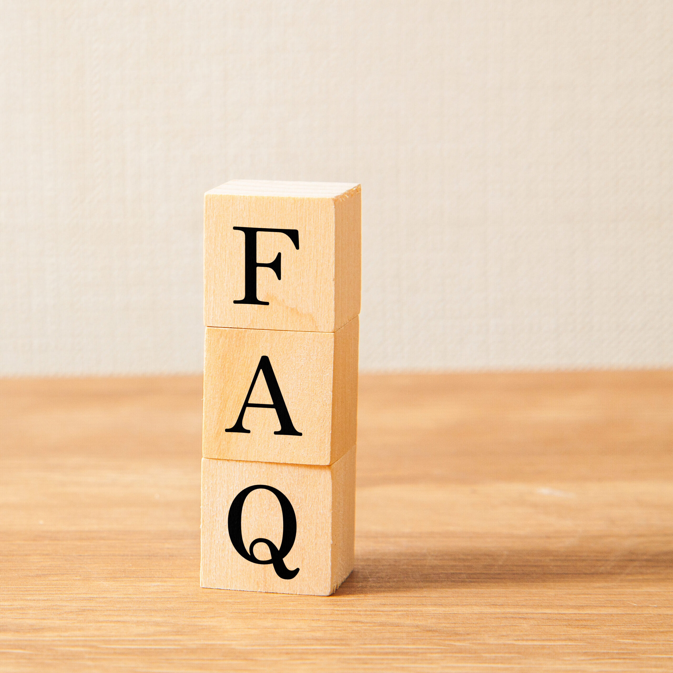 Three wooden blocks stacked vertically on a wooden surface, each with a large black letter spelling "FAQ" from top to bottom, against a neutral background.